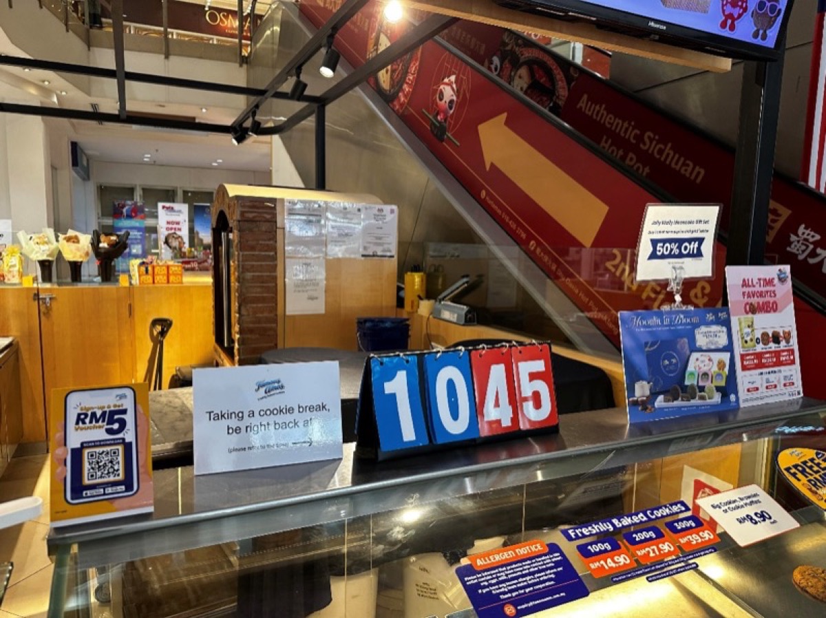 A cookie counter with a sign reading "Taking a cookie break, be right back at" next to a flip-number board set to 10:45